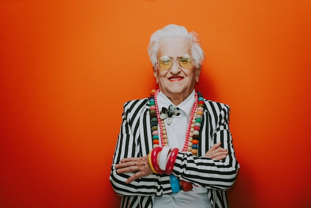 Portrait of stylish senior woman wearing colorful jewelry standing against red background