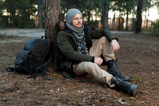 Portrait stylish serious traveler man with a beard in pine forest