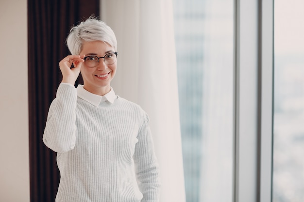 Portrait of stylish smiling young woman in white sweater and glasses