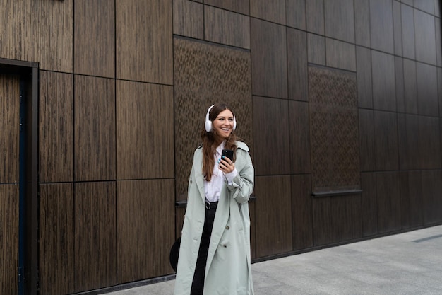 Portrait of a stylish young woman in headphones using a mobile phone against the background of a