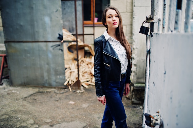 Portrait of stylish young woman wearing on leather jacket and ripped jeans at streets of city