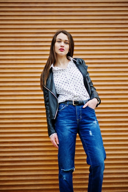 Portrait of stylish young woman wearing on leather jacket and ripped jeans at streets of city