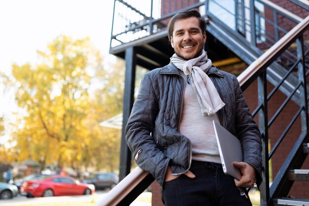 Portrait of a successful adult man with a wide smile on his face standing on the stairs against the