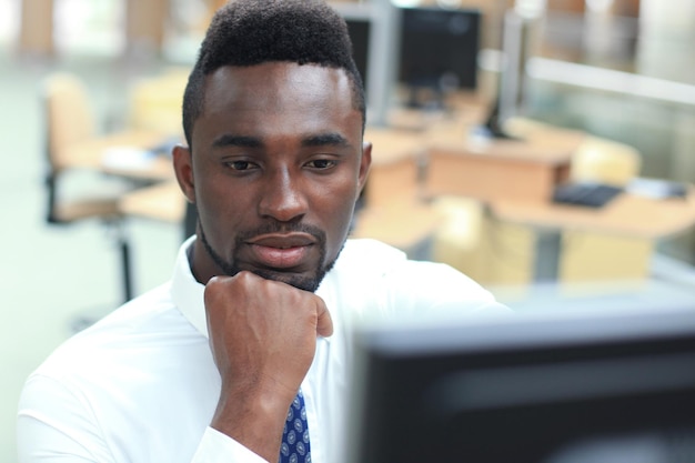 Portrait of successful African-American businessman sitting at desk with computer in office.