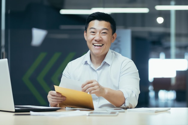 Photo portrait of successful asian investor man puts money money cash in envelope smiling and looking at