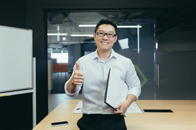 Portrait of successful asian teacher man in modern classroom looking at camera and smiling wearing