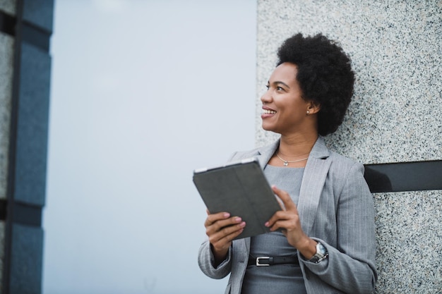 Portrait of a successful black business woman using digital\
tablet during quick break in front a corporate building.