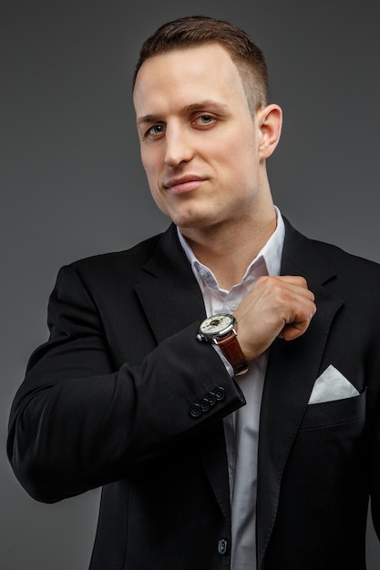 Portrait of successful business man in a black suit on grey background.