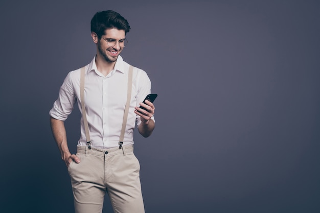 portrait of successful business man good mood holding telephone hands read work email dressed formalwear shirt suspenders trousers specs .