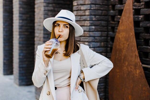 Portrait of successful business woman holding cup of cold drink in hand on her way to work on city street