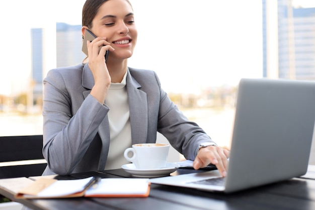 Portrait of successful business woman talking on the phone and smiling while working in the modern cafe.