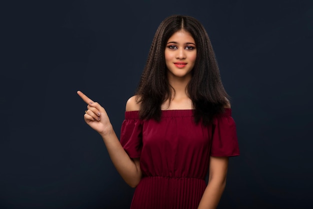 Portrait of a successful cheerful young girl pointing and presenting something with hand or finger with a happy smiling face