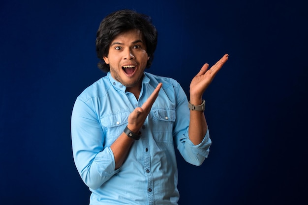 Portrait of a successful cheerful young man pointing and presenting something with hand or finger with a happy smiling face