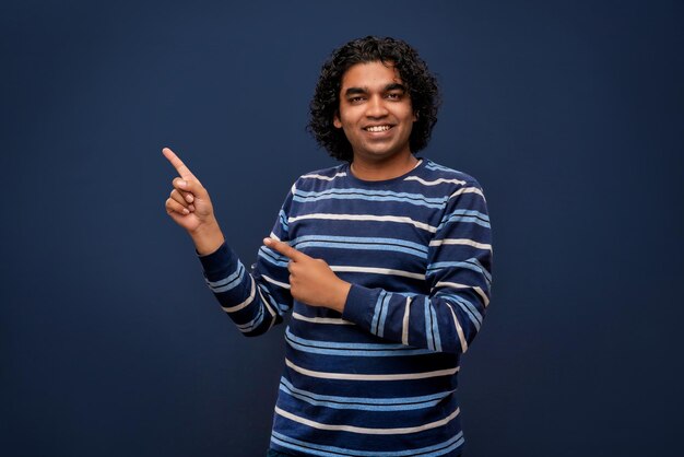 Portrait of a successful cheerful young man pointing and presenting something with hand or finger with a happy smiling face