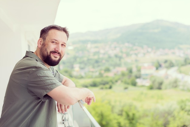 Foto ritratto di giovane hipster felice di successo in piedi su un balcone moderno con vista sulla città sullo sfondo