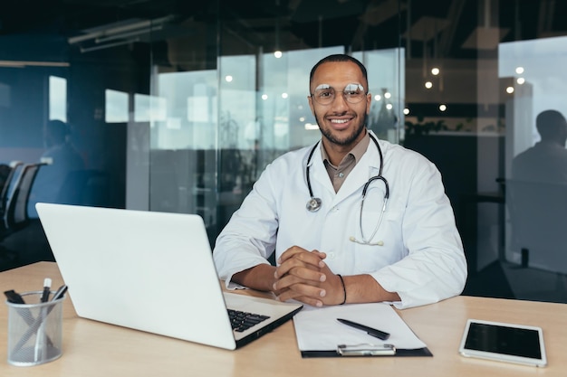 Ritratto di successo medico maschio ispanico sorridente e guardando il medico della fotocamera in abito medico