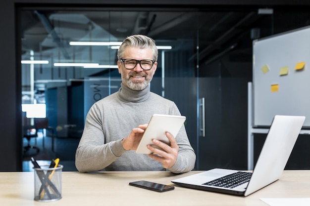 Portrait of successful programmer team leader mature grayhaired engineer testing new app on tablet