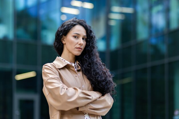 Portrait of successful proud woman boss outside office building hispanic satisfied with work looking