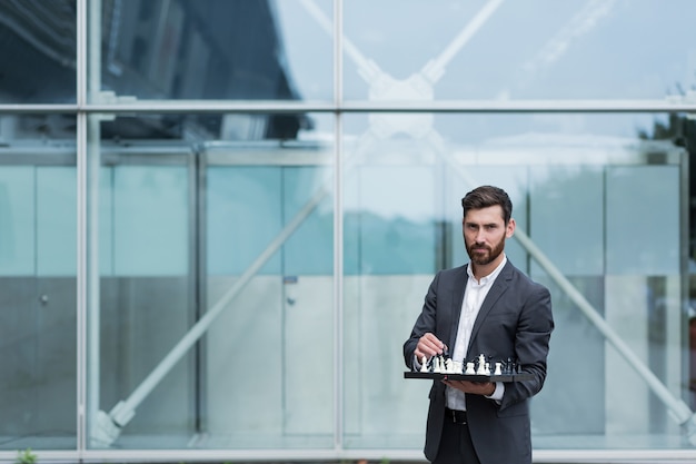 Portrait of a successful serious businessman holding a board with chess in his hands offers to take a step