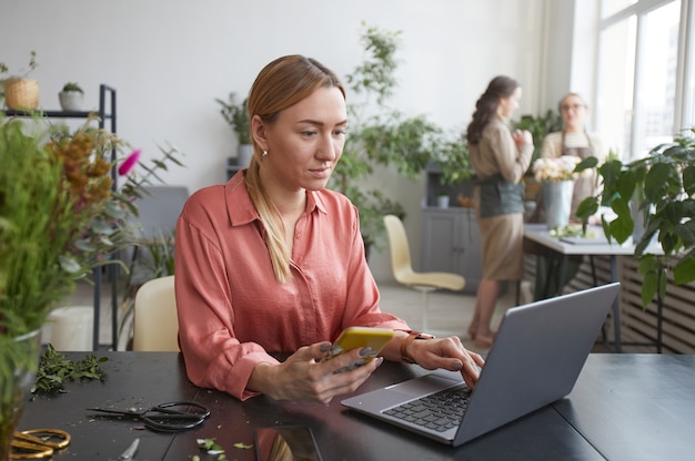 Portrait of successful young businesswoman using computer in flower shop while managing small business, copy space