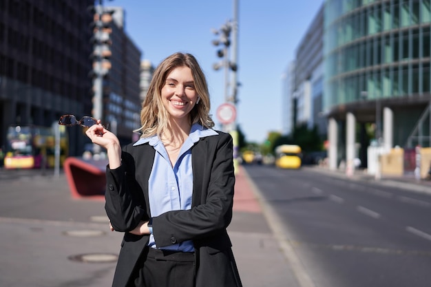 Portrait of successful young company ceo businesswoman in black\
suit standing on sunny street and sm