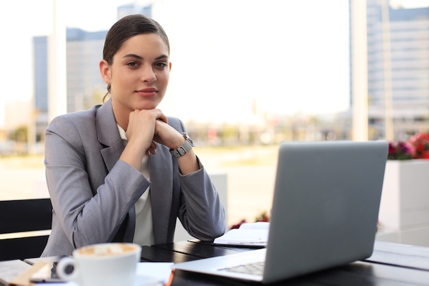 Portrait of successful young woman with laptop in street cafe.