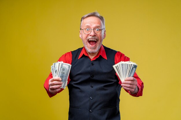 Portrait of super excited senior mature man who just won lots of money. Isolated on yellow background. Positive emotions. Facial expressions. Closeup.