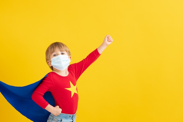 Portrait of super hero kid against yellow paper wall.