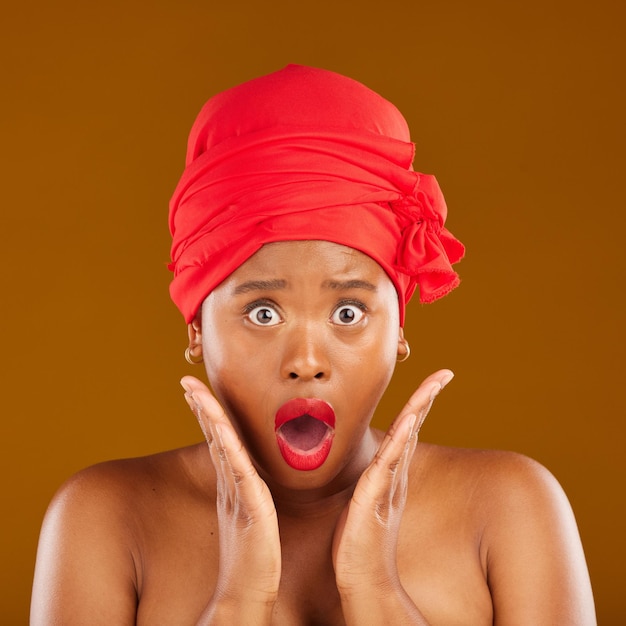 Portrait surprise and black woman with makeup cosmetics or head wrap against a brown studio background Face female person or model shocked creative and dermatology with news self care and shine