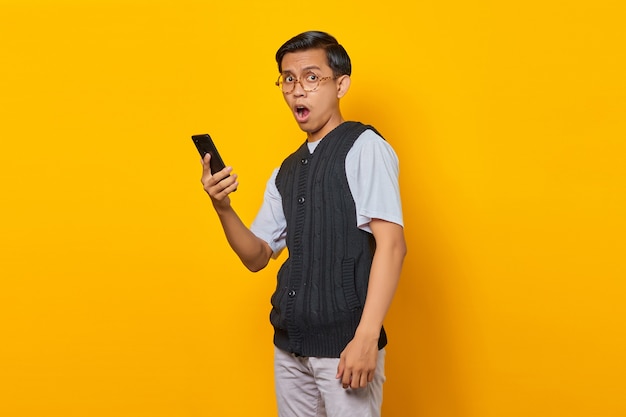 Portrait of surprised asian man looking ahead with open mouth and holding smartphone