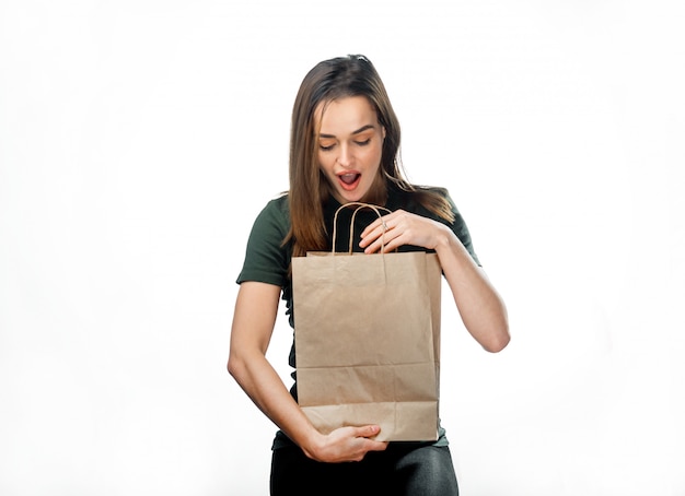 Portrait of surprised attractive long-haired woman looking into paper bag on white