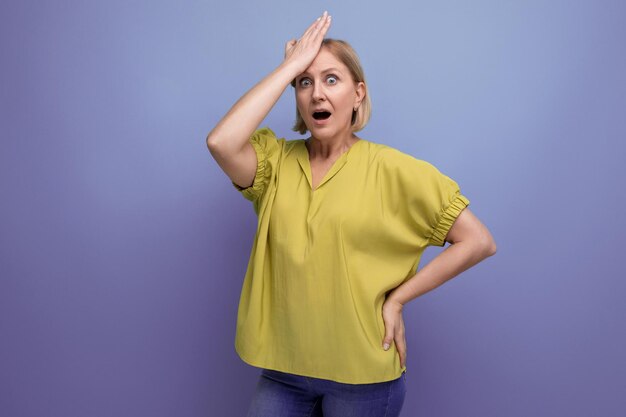 Portrait of surprised blond middle aged woman in yellow tshirt on studio background