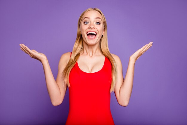 Portrait of surprised blonde girl wearing red swimsuit isolated on violet