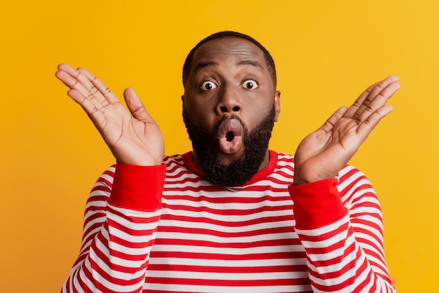 Portrait of surprised bug-eyed young dark-skinned man hands cheeks open mouth on yellow background