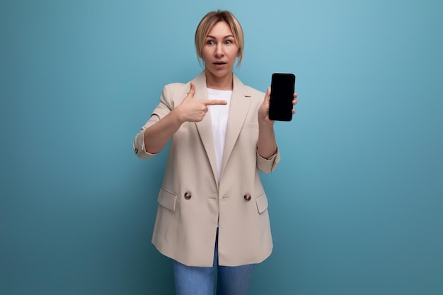 Portrait of surprised business woman in store showing smartphone mockup in studio with copy space