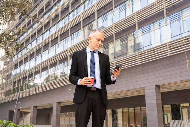 Foto ritratto di un uomo d'affari sorpreso che usa un'app sul suo smartphone e in piedi all'aperto
