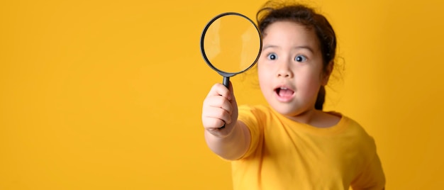 Ritratto di piccola ragazza asiatica sveglia sorpresa che guarda tramite una lente d'ingrandimento. concetto di educazione.