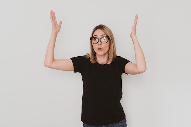 Portrait of surprised european woman in casual clothers and glasses raised her hands up. On white background. Hand gestures