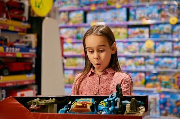 Portrait of surprised girl child looking at new collection of toys in store