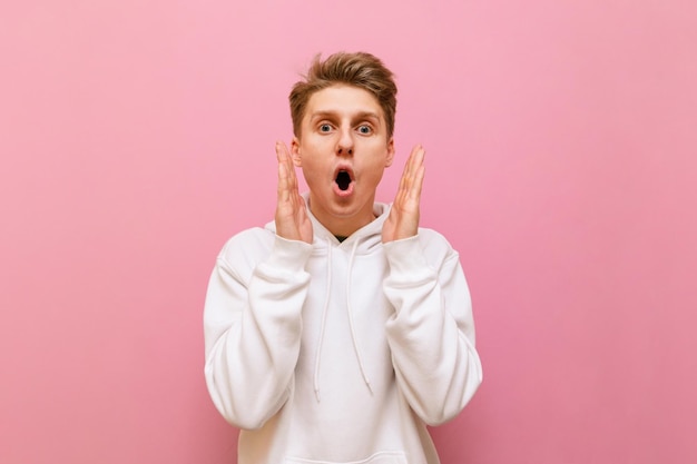 Portrait of surprised guy in white hoodie looking into camera with crazy face Copy space