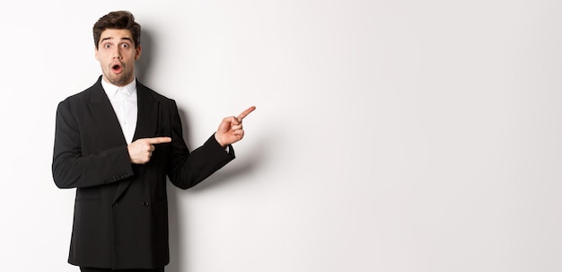 Photo portrait of surprised handsome man with beard wearing black suit open mouth and pointing fingers rig