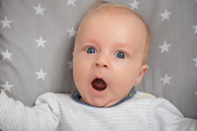 Portrait of surprised newborn baby with open mouth closeup Cut child with blue eyes looking