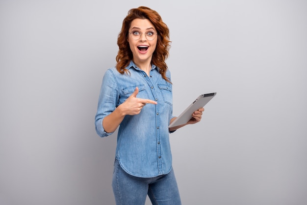 Portrait of surprised woman use tablet search social networking news impressed scream wow omg point index finger wear style stylish trendy denim jeans shirt isolated over grey color wall