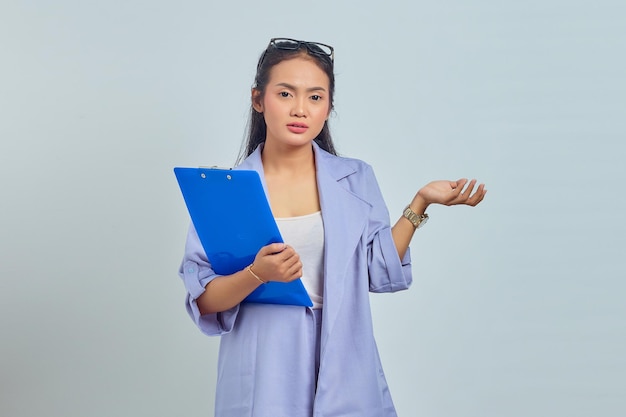 Portrait of surprised young Asian business woman holding document folder and showing copy space in palm isolated on purple background