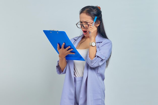 Ritratto di giovane donna d'affari asiatica sorpresa guardando l'elenco di lavoro negli appunti isolato su sfondo viola