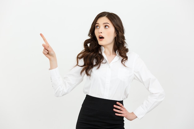 Portrait of surprised young businesswoman pointing finger away to copy space.