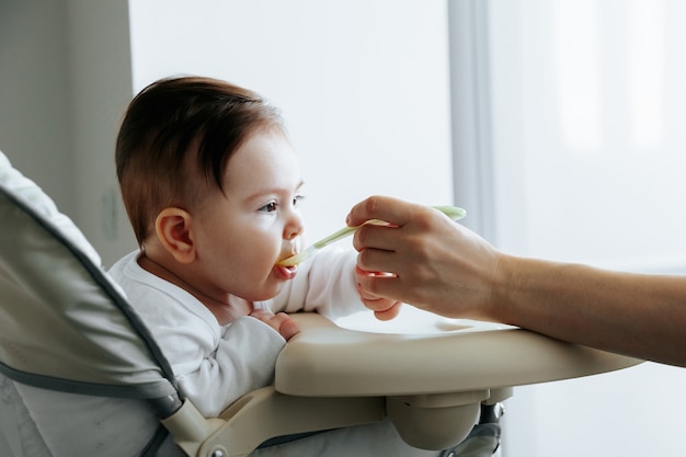 Portrait of a sweet child who is fed baby food from a spoon side view caucasian mother feeding her b...