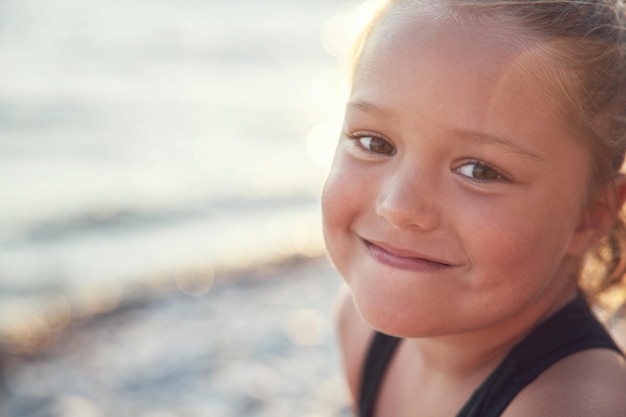 Портрет загорелой маленькой девочки в лучах солнца на фоне моря