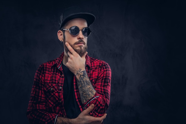 Photo portrait of tattoed, bearded male with a tattoo on arms, in sunglasses and flannel shirt.