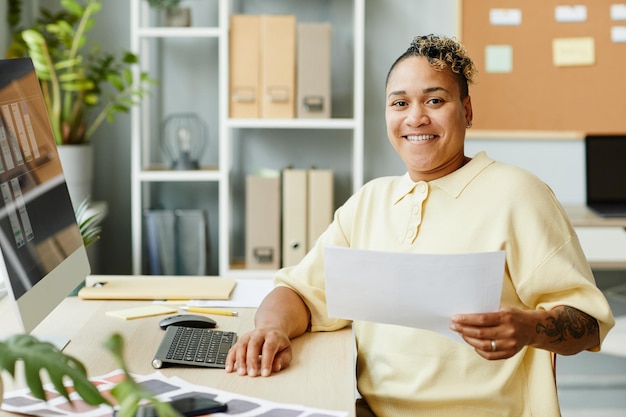 Portrait of tattooed black woman designing websites and mobile
apps in office and smiling at camera